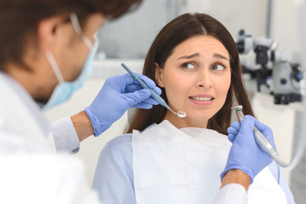 Woman with brown hair looking at anxiously at dentist approaching trying to examine her